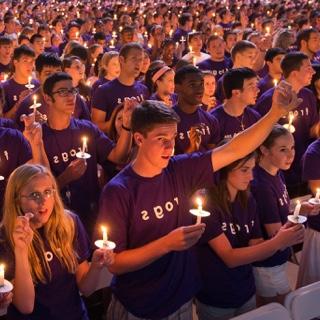 A large group of students — all with purple Go Frogs shirts and each with a lit candle — gather during the Chancellor's Assembly