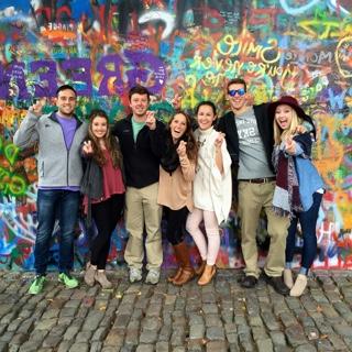 Seven TCU students studying abroad stand in front of a brightly spray-painted graffitti wall on a cobblestone street in Prague.