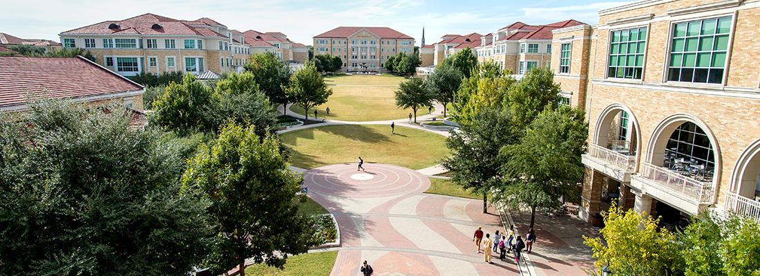 High up view of the TCU campus commons with scattered groups of pedestrians. Frog Fountain is visible in the distance and a huge horned frog logo can be seen on the brick walkway