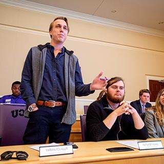A male student stands to speak at a TCU student government meeting in the chambers of the student union.